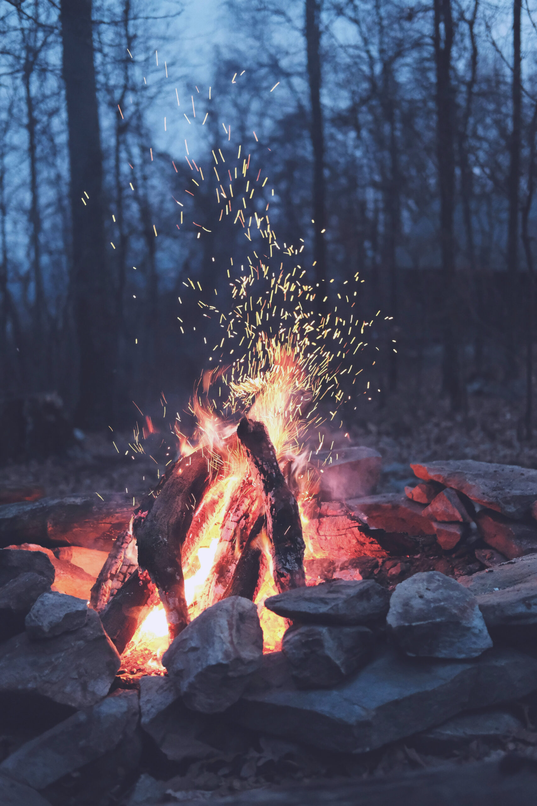Warm, glowing campfire sending up sparks at dusk